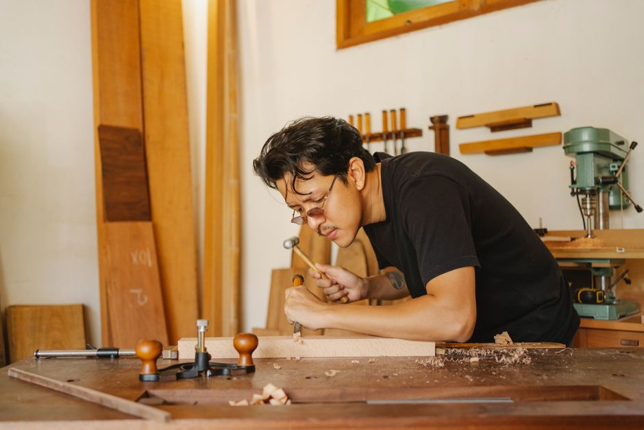 Skilled artisan working intently at a woodworking bench, crafting furniture indoors.