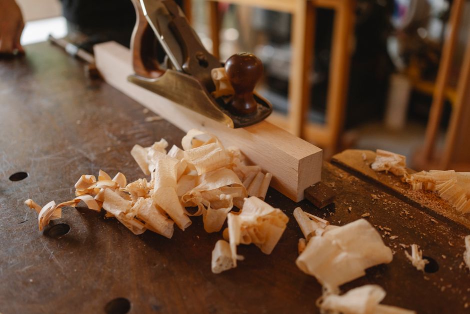 Workbench of joiner with plane on timber plank and wood shavings in daylight